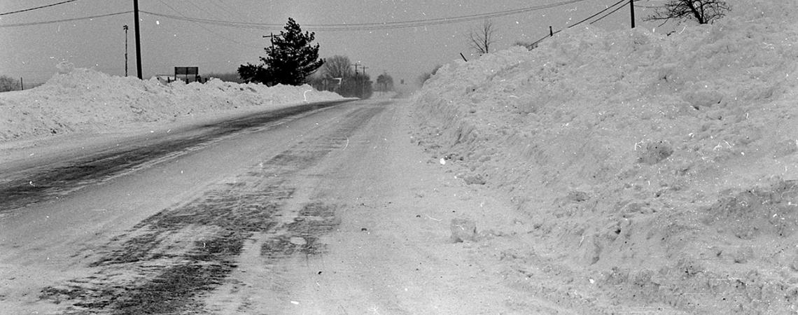 A snow-covered road with large piles of snow on either side of it.