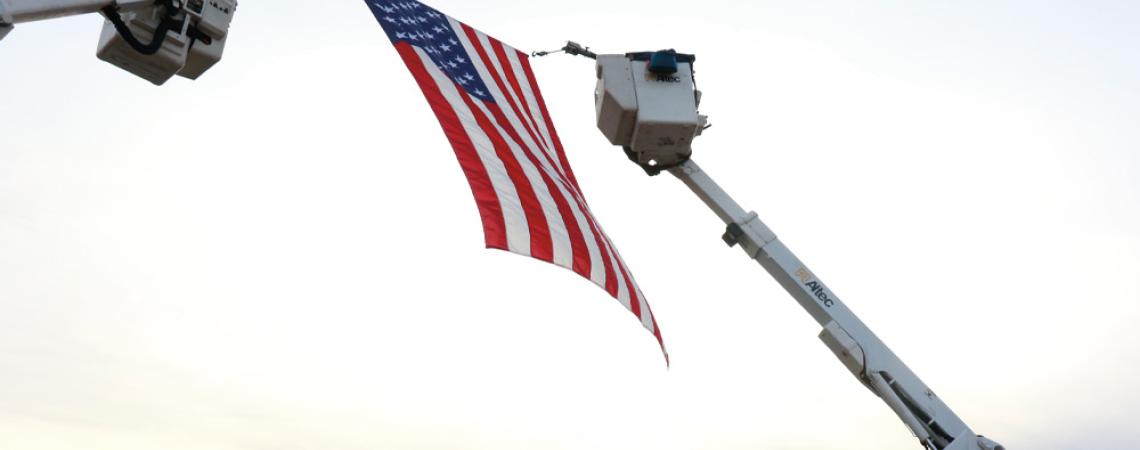 An American flag being held by two bucket trucks