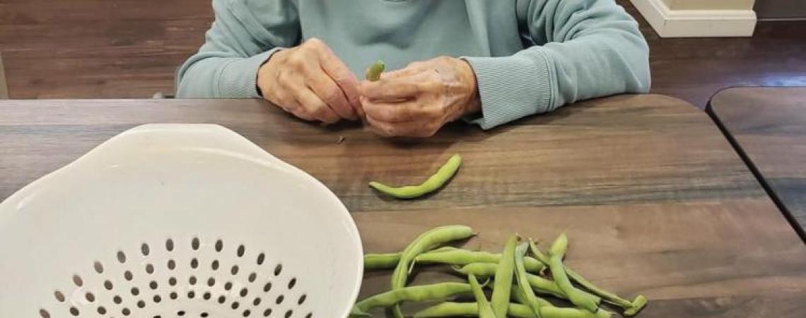 A resident of Woodland Country Manor helping snap green beans for a meal.