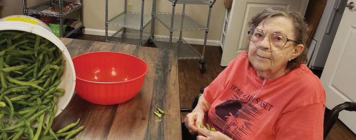 A resident of Woodland Country Manor helping snap green beans for a meal.