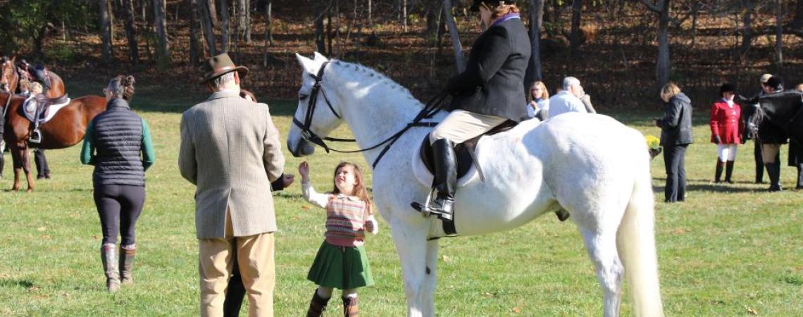 A young girl petting a horse after a fox hunt. 