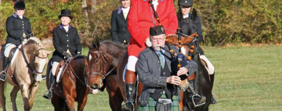 A bagpiper leading a group of equestrians before a fox hunt.