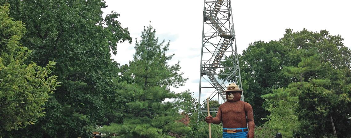 A 15-foot-tall statue of Smokey Bear standing in front of a fire tower