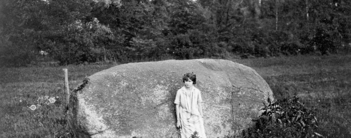 A black and white photo of a person standing in front of a large boulder