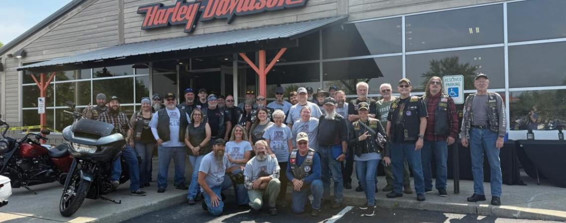 A large group of people posing with their motorcycles under a Harley-Davidson sign