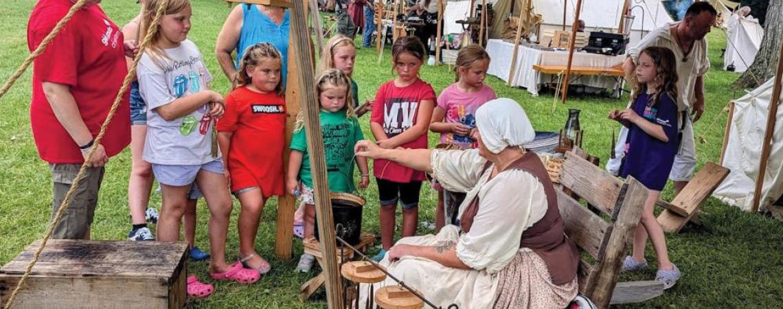 A group of kids making candles at a historic fair