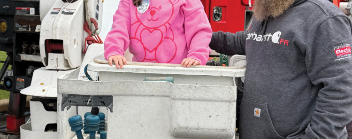 A man standing beside a young girl in the bucket of an electric bucket truck