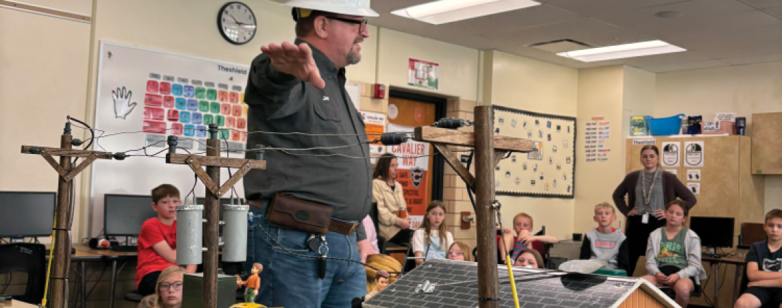A man wearing a hard hat and showing an electric tabletop display to students in a classroom